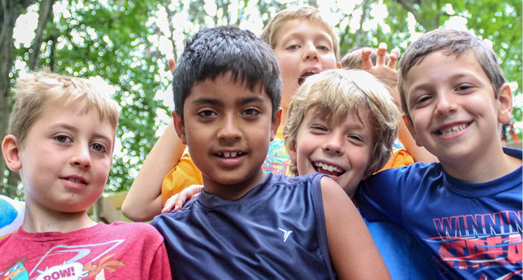 Group of boys smiling for the camera outside with trees in background.