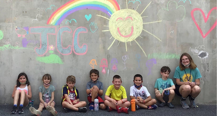 Group of children and counselor outside against grey wall with chalk artwork.