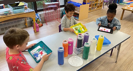 Three children seated at a table doing arts and crafts.