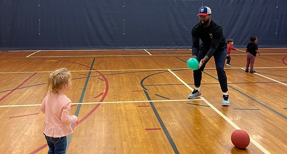 Little girl playing catching with male coach in gymnasium.