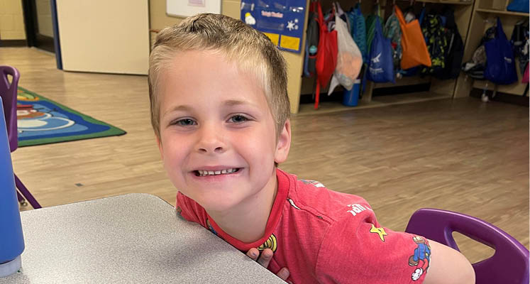 Young boy seated at a table smiling.